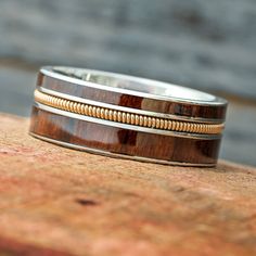 two wedding bands with wood and gold inlays sit on top of a piece of wood