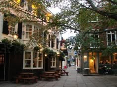 an empty street with tables and benches on the sidewalk in front of some buildings at dusk