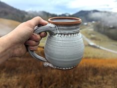 a hand holding a ceramic mug in the middle of a field