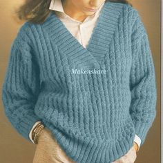 a woman wearing a blue sweater and tan pants with her hands in her pockets, looking to the side