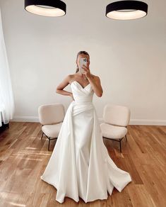 a woman in a white dress taking a selfie with her cell phone while standing on a hard wood floor