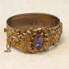 This antique Victorian etched gold plate bangle bracelet is heavy with details and a beautiful purple glass stone.  This is quite a statement piece from an amazing period of time long ago. This bangle really depicts the style and appreciation of craftsmanship of the time period it was made in. What an unusual and wonderful piece to own and enjoy!Antique BraceletVictorianGlassGold PlatedBangle BraceletDimensions: Will fit a 7" inch wrist and is 1" inch widePlease read our shop policies prior to p Luxury Victorian Etched Bangle, Antique Gold Bangle With Antique Finish, Elegant Bangle With Antique Finish, Vintage Purple Bangle Jewelry, Elegant Bangle Jewelry With Antique Finish, Elegant Bangle Bracelet With Antique Finish, Elegant Antique Finish Bangle Bracelet, Elegant Antique Finish Bangle, Antique Gold Bracelet In Antique Style