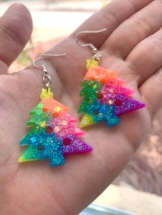 a pair of colorful earrings in the palm of someone's hand, with glitter on them