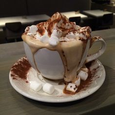 a white cup filled with hot chocolate and marshmallows on top of a saucer