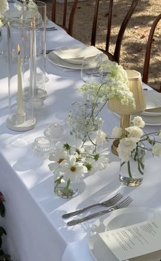 the table is set with white flowers and silverware