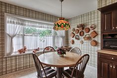 a dinning room table and chairs in front of a window with wall hangings