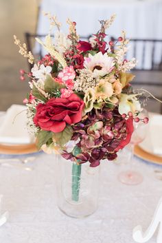 a vase filled with lots of flowers on top of a white tablecloth covered table