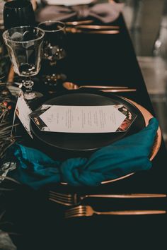 a table set with black plates and silverware, blue napkins and wine glasses