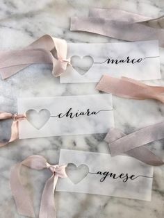 three place cards with hearts and ribbons tied to them on a marble countertop in the shape of heart