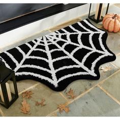 a black and white spider web rug on the ground next to a lantern with pumpkins