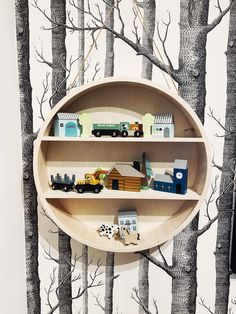 there is a shelf with toy cars on it in the tree - lined wallpaper