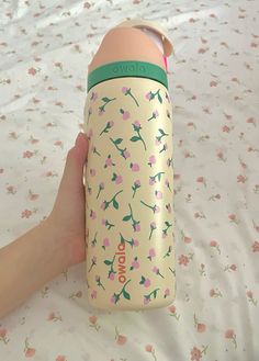 a hand holding a pink and green water bottle on top of a floral print sheet