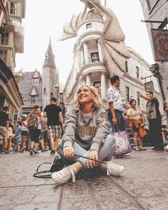 a woman sitting on the ground in front of a building with a dragon statue behind her