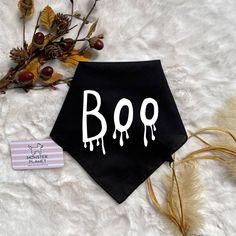 a black bandana with the word boo painted on it next to dried flowers and a tag