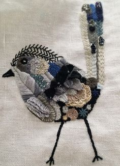 a close up of a bird made out of knits and flowers on a white cloth