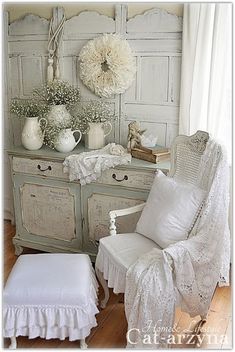 a white chair and ottoman in front of a dresser with flowers on the top shelf