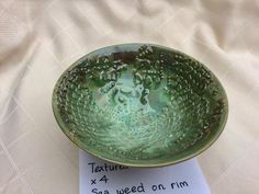 a green bowl sitting on top of a table next to a piece of white paper