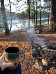 a person holding a coffee cup in front of a campfire