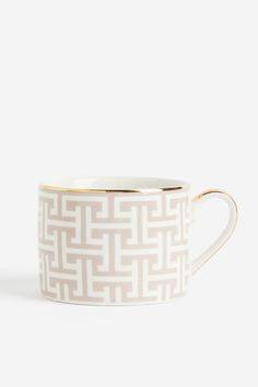 a white and gold coffee cup with an intricate design on the inside, sitting against a white background