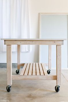 a wooden table sitting on top of a floor next to a white wall and window