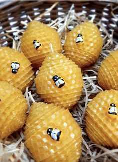 yellow honey balls with black and white faces on them in a wicker basket filled with straw