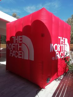 the north face inflatable tent is set up on a patio with red flowers and greenery