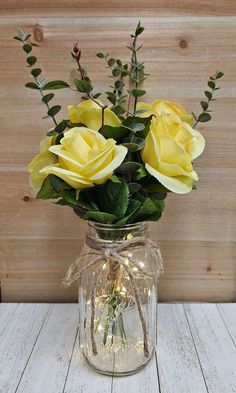 a glass jar filled with yellow roses and greenery