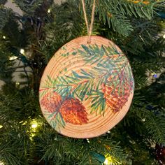 a wooden ornament with pine cones on it hanging from a christmas tree branch