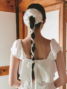 a woman wearing a white dress with a long braid in it's hair, looking at herself in the mirror