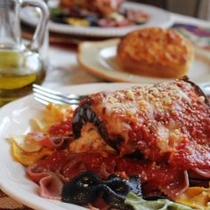 a white plate topped with lasagna covered in sauce and cheese next to bread