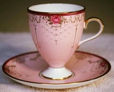 a pink cup and saucer on a white tablecloth with gold trimmings