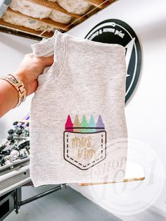 a person holding up a t - shirt with the words happy camp on it and colorful crayons