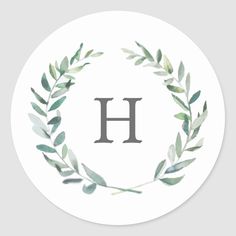 the letter h is surrounded by green leaves and branches on a white round sticker