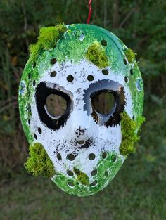 a mask with moss growing on it is hanging from a wire in front of some trees