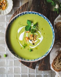 a bowl filled with green soup on top of a wooden table next to slices of bread