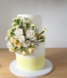 a white and yellow wedding cake with flowers on the top is sitting on a table