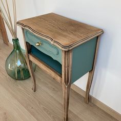 a wooden table sitting next to a green vase on top of a hard wood floor