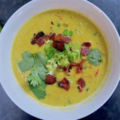 a white bowl filled with soup and garnished with cilantro, celery, and bacon