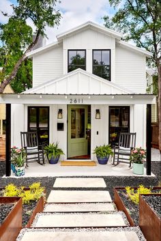 a small white house with two rocking chairs on the front porch and an open door