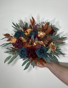 a hand holding a bouquet of flowers on a white wall with leaves and foliage around it