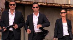 two men and a woman are walking down the street with one man in a suit