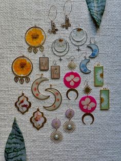 many different types of earrings are arranged on a table top, including one with a green leaf and the other with an orange flower