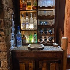 an old wooden cabinet with bottles and glasses on it's shelf next to a stone wall