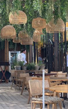 an outdoor dining area with wooden tables and wicker hanging from the ceiling, surrounded by greenery