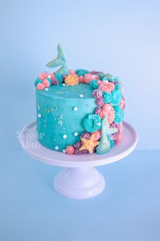 there is a blue cake with pink and green decorations on the top, sitting on a white pedestal