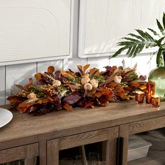 a wooden table topped with a vase filled with flowers and candles next to a plant