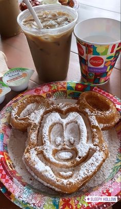 a mickey mouse waffle on a colorful plate next to a cup of coffee and drink