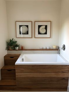 two framed pictures above a white bathtub in a bathroom with wooden steps leading up to the tub