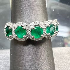 an emerald and diamond three stone ring on a silver napkin with white diamonds around it