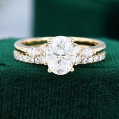 an engagement ring with three stones on top and two bands around the band, sitting on a green velvet cushion